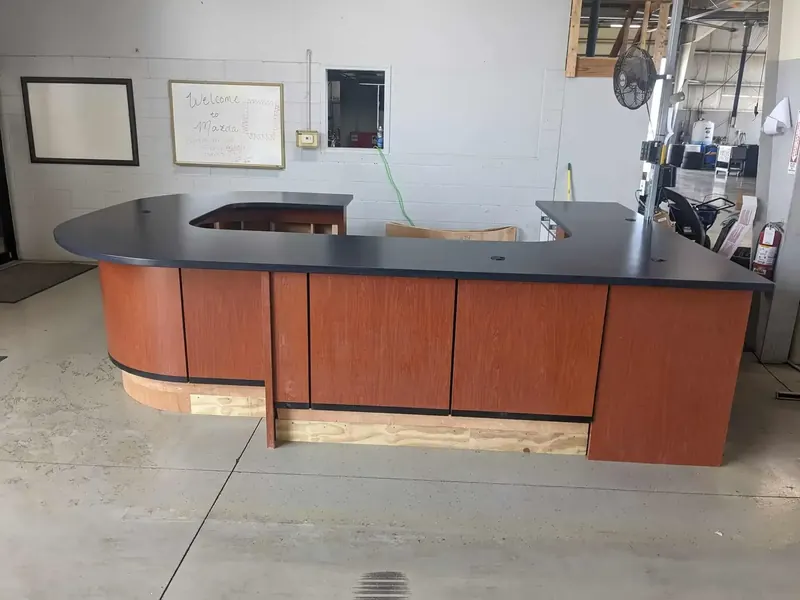 Curved commercial reception desk with cherry woodgrain laminate front and black laminate top, under construction in the shop