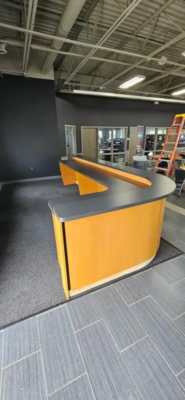 L-shaped reception desk in maple woodgrain laminate with a dark grey laminate top