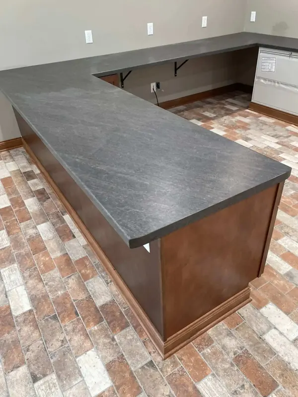 L-shaped basement bar with a charcoal slate-look laminate top and cherry-stained bar front