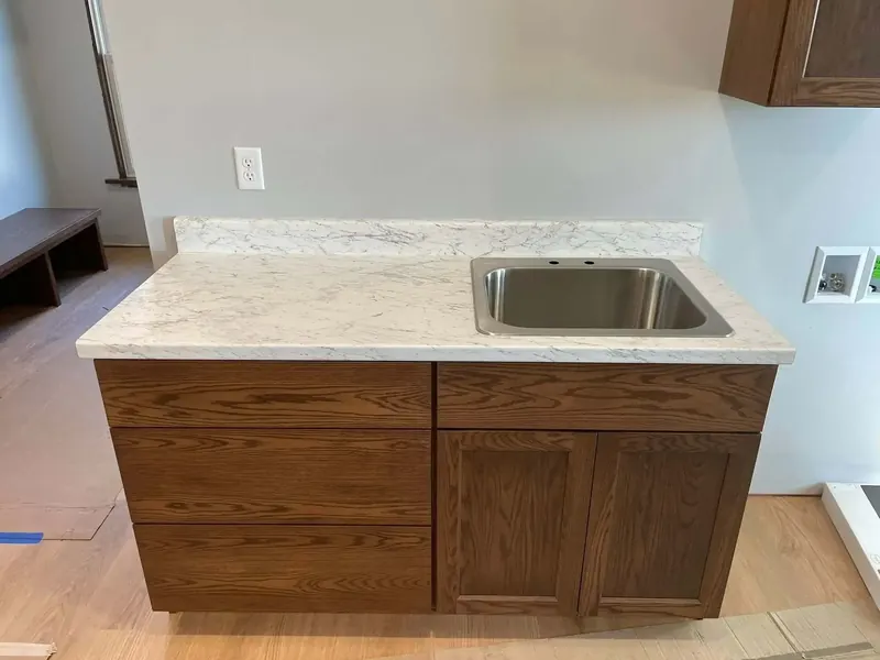 Laundry room counter in white marble-look laminate with a stainless utility sink and oak cabinets