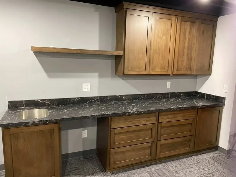 Black marble-look laminate counter with white veining, a round bar sink and honey-stained cabinets
