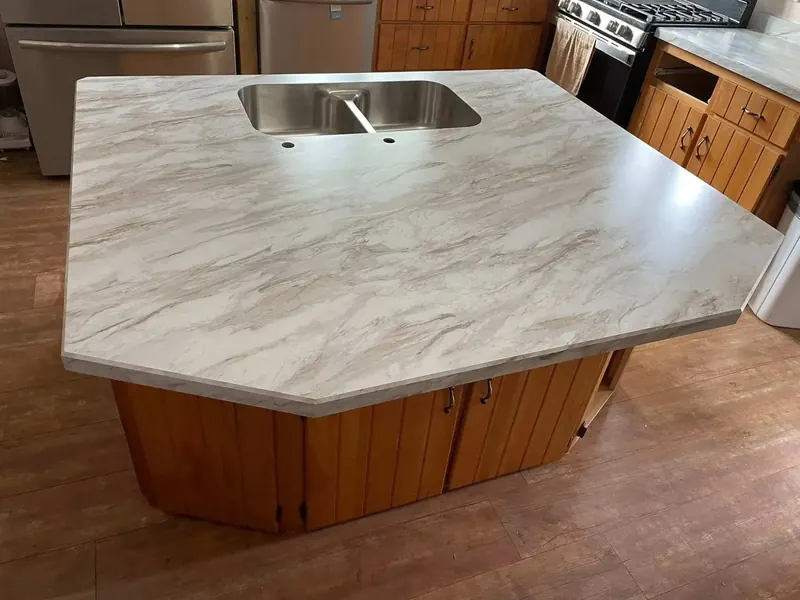 Angled kitchen island in white and taupe marble-look laminate with a stainless double-bowl sink