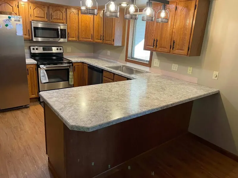 U-shaped kitchen peninsula in beige speckled granite-look laminate with oak cabinets