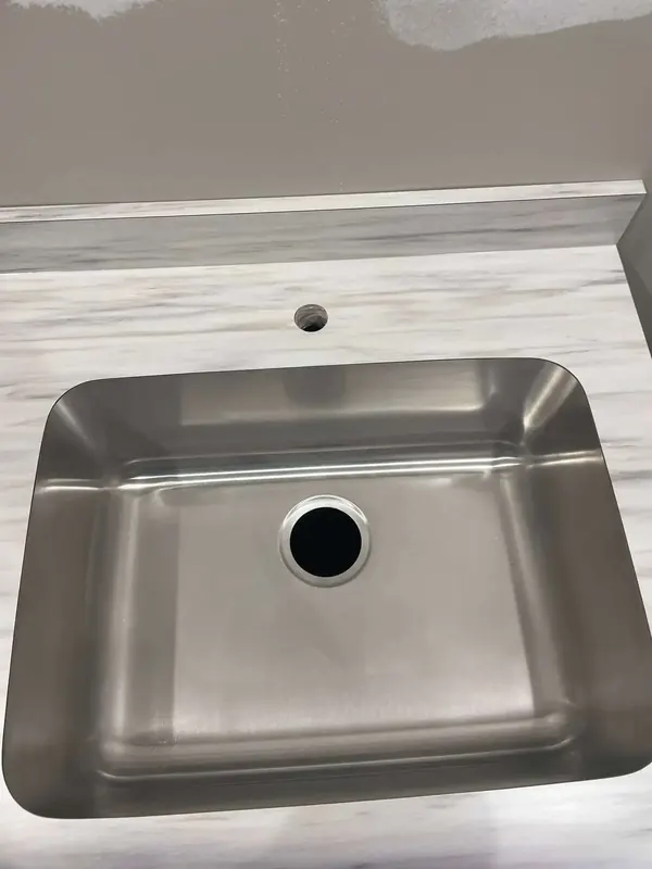 Close-up of a single-bowl stainless sink set into white marble-look laminate