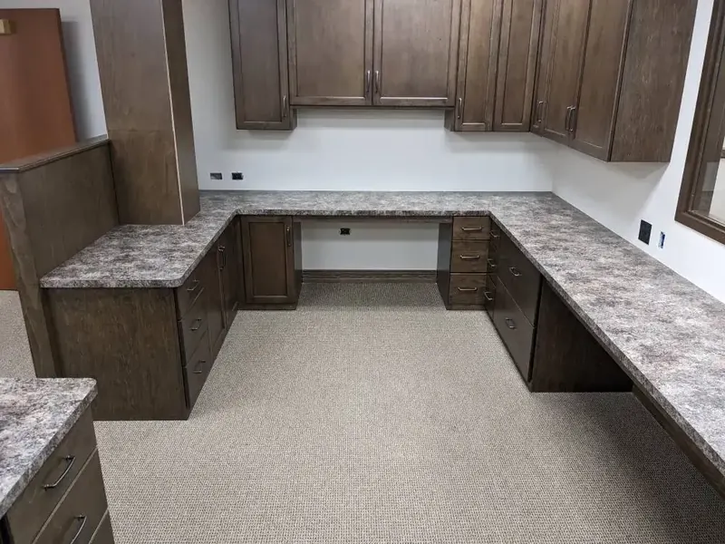 U-shaped home office desk in grey speckled granite-look laminate with dark stained cabinetry