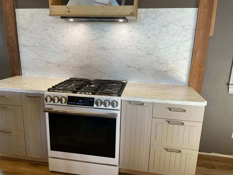 White marble-look laminate countertop with full-height matching backsplash behind a gas range