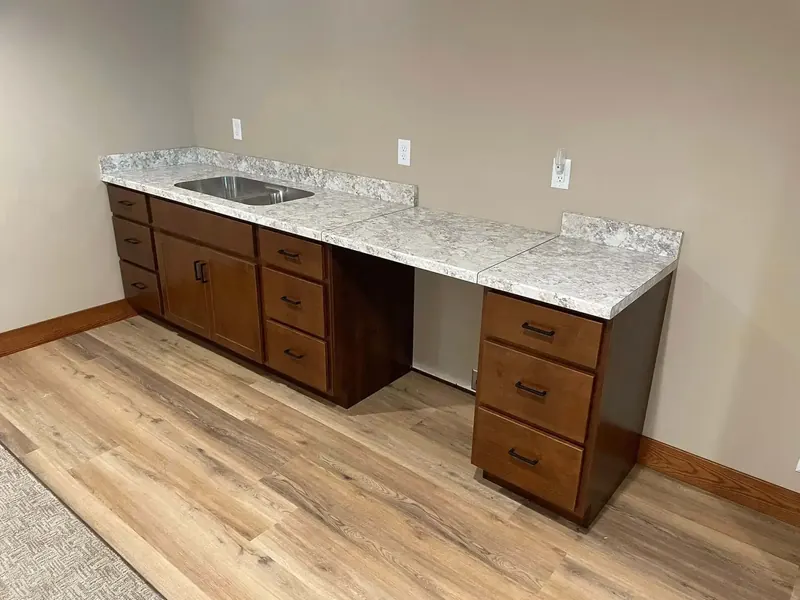 Break room counter in speckled grey laminate with a stainless bar sink and open knee space