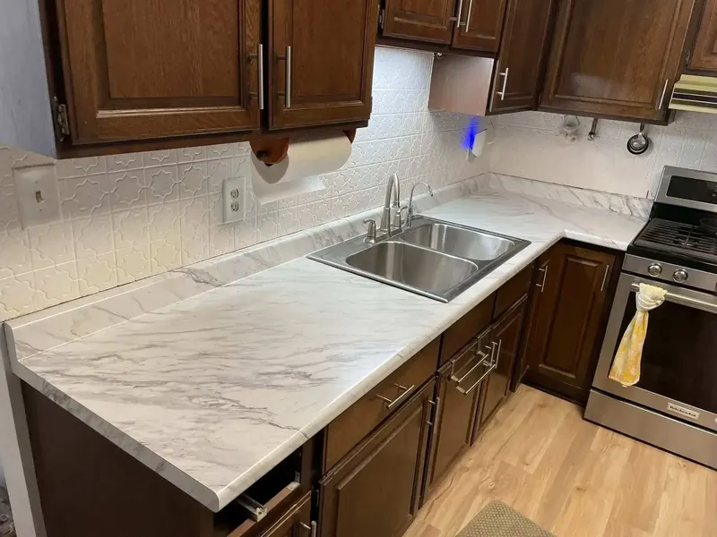 White marble-look laminate kitchen counter with a stainless double-bowl sink and dark cabinets